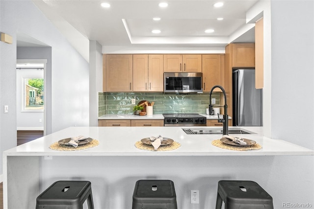 kitchen featuring appliances with stainless steel finishes, recessed lighting, a kitchen bar, decorative backsplash, and light countertops