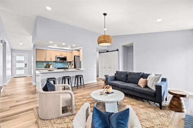 living room featuring a barn door, light wood finished floors, baseboards, and recessed lighting