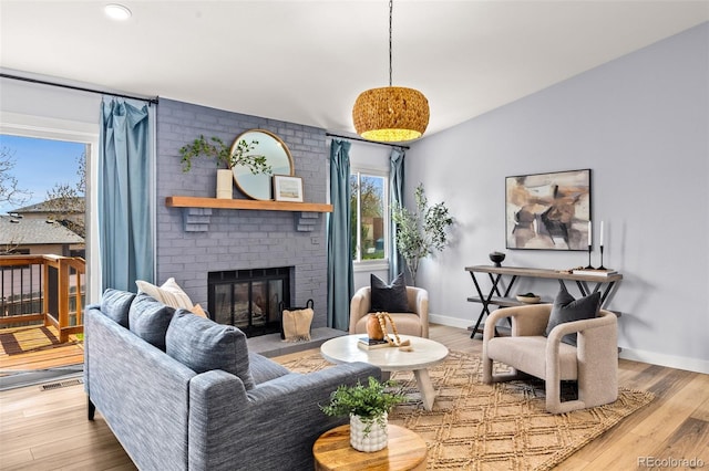 living room with a brick fireplace, baseboards, and wood finished floors