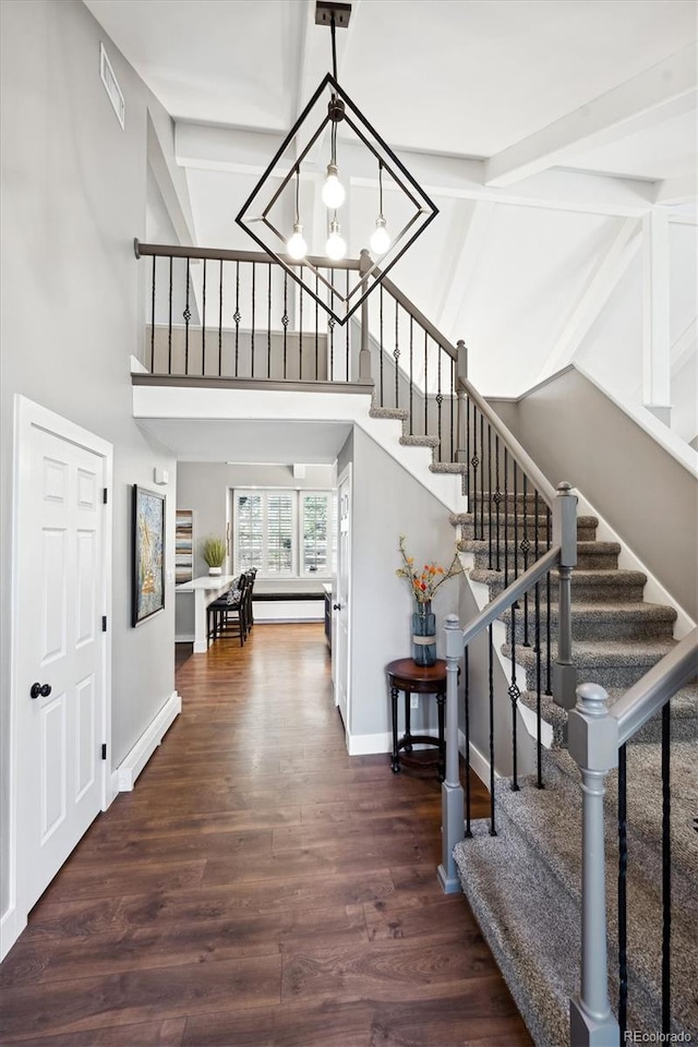 entrance foyer with dark hardwood / wood-style floors, an inviting chandelier, a high ceiling, baseboard heating, and beam ceiling