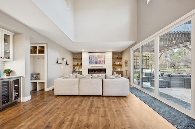 living room featuring beverage cooler, a fireplace, wood-type flooring, and a high ceiling