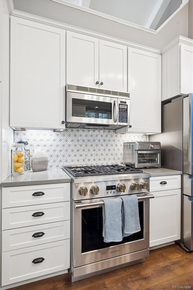 kitchen featuring vaulted ceiling, appliances with stainless steel finishes, tasteful backsplash, white cabinetry, and dark wood-type flooring