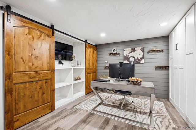 office area with a barn door, built in features, light hardwood / wood-style floors, and wood walls