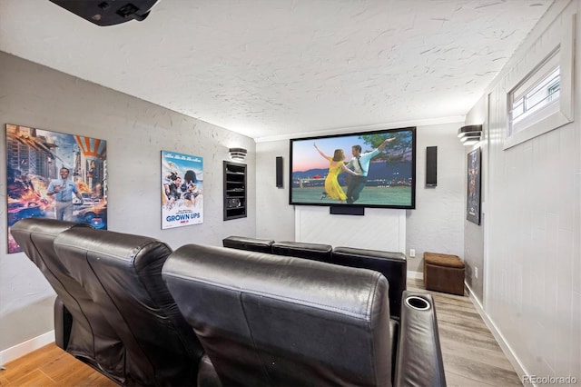 home theater room with baseboards, a textured wall, light wood-style flooring, and a textured ceiling