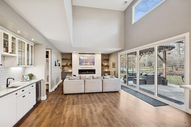 living area featuring a high ceiling, a fireplace, baseboards, and wood finished floors