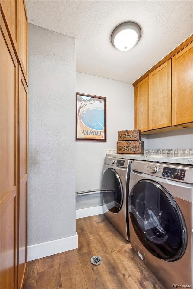 clothes washing area with cabinet space, washing machine and dryer, baseboards, and wood-type flooring