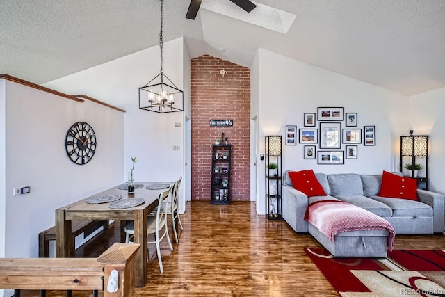 living room with dark wood-type flooring, lofted ceiling, ceiling fan with notable chandelier, and a textured ceiling