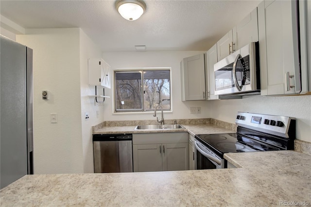 kitchen with a textured ceiling, light countertops, appliances with stainless steel finishes, and a sink