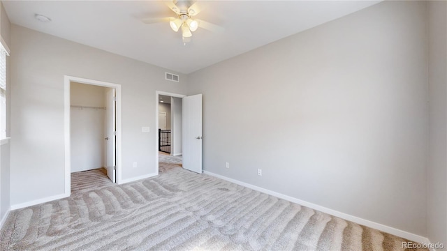 unfurnished bedroom featuring light colored carpet, a walk in closet, ceiling fan, and a closet