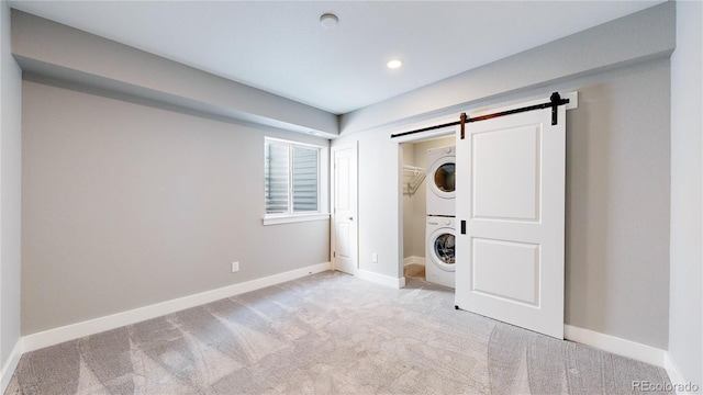 spare room featuring a barn door, stacked washer and clothes dryer, and light carpet