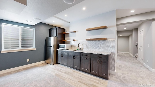 kitchen featuring light stone countertops, dark brown cabinets, appliances with stainless steel finishes, sink, and light colored carpet