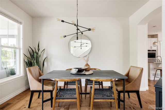 10069 E 28th Ave, Denver, CO 80238 - dining room featuring arched walkways, a chandelier, and light wood-style floors