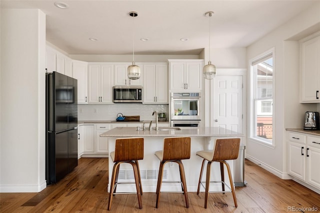 10069 E 28th Ave, Denver, CO 80238 - kitchen with black appliances, white cabinetry, light wood finished floors, a kitchen bar, and decorative backsplash