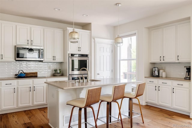 10069 E 28th Ave, Denver, CO 80238 - kitchen featuring stainless steel appliances, decorative backsplash, light wood-type flooring, white cabinets, and recessed lighting