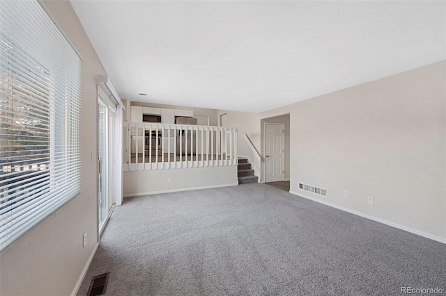 carpeted empty room featuring stairs, visible vents, and baseboards