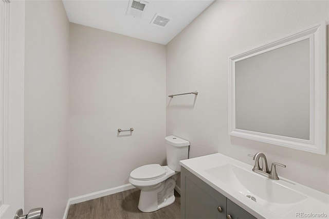 bathroom with visible vents, toilet, vanity, wood finished floors, and baseboards