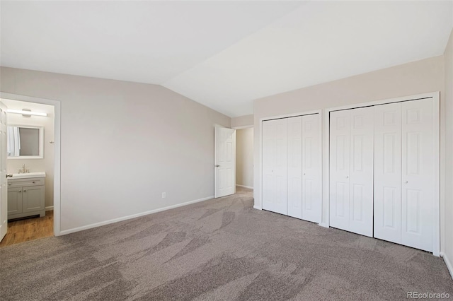 unfurnished bedroom with multiple closets, lofted ceiling, carpet floors, and ensuite bath