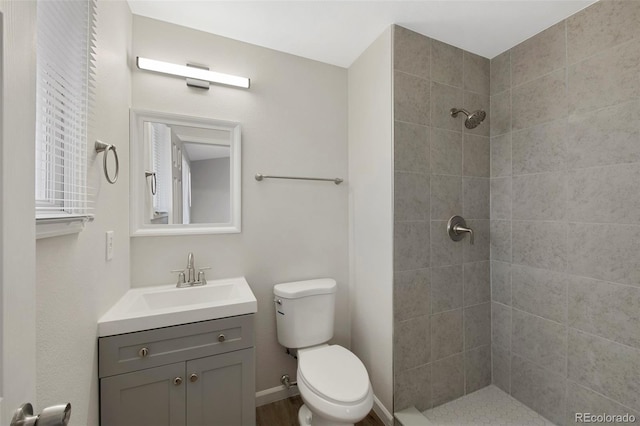 full bathroom with toilet, baseboards, tiled shower, and vanity