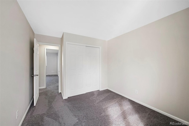 unfurnished bedroom with dark colored carpet, a closet, and baseboards