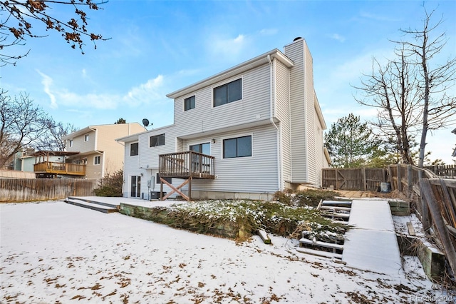 snow covered rear of property with a deck, a fenced backyard, and a chimney