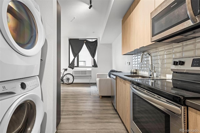 kitchen featuring appliances with stainless steel finishes, light wood-type flooring, backsplash, sink, and stacked washer and clothes dryer