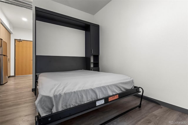 bedroom featuring wood-type flooring and stainless steel refrigerator