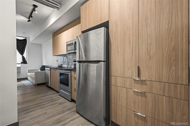 kitchen with light brown cabinetry, rail lighting, stainless steel appliances, and light hardwood / wood-style floors