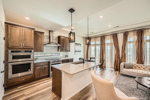 21701 E 50th Dr, Aurora, CO 80019 - kitchen featuring wall chimney exhaust hood, stainless steel appliances, light wood-style floors, light countertops, and a sink