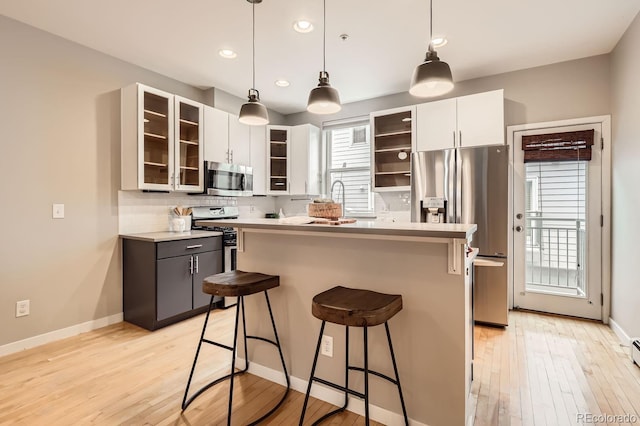 kitchen featuring tasteful backsplash, a kitchen island, stainless steel appliances, light wood-type flooring, and a kitchen bar