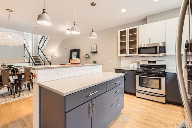 kitchen with light countertops, appliances with stainless steel finishes, gray cabinets, a center island, and light wood finished floors