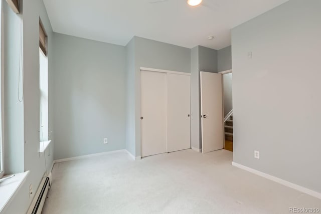 unfurnished bedroom featuring baseboards, baseboard heating, a closet, and light colored carpet