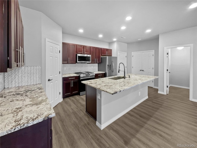 kitchen featuring sink, appliances with stainless steel finishes, a kitchen island with sink, dark hardwood / wood-style floors, and light stone counters