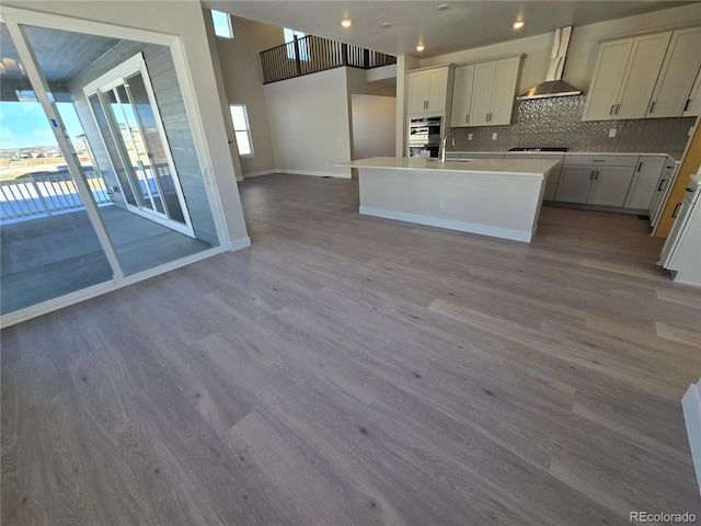 kitchen featuring sink, wall chimney range hood, gas stovetop, hardwood / wood-style floors, and a kitchen island with sink