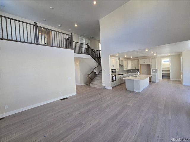 unfurnished living room featuring a towering ceiling, sink, and light hardwood / wood-style flooring