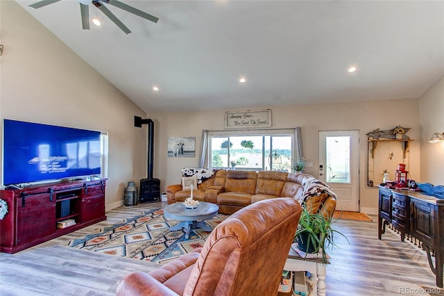 living room featuring lofted ceiling, ceiling fan, light hardwood / wood-style flooring, and a wood stove