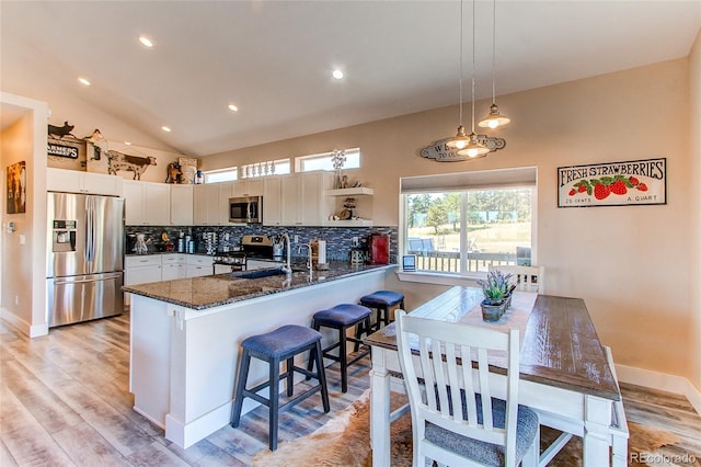 kitchen with a breakfast bar area, stainless steel appliances, hanging light fixtures, kitchen peninsula, and white cabinets