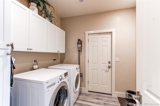 clothes washing area featuring washing machine and dryer, light wood-type flooring, and cabinets