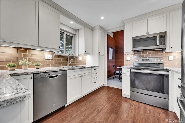 30334 Roan Dr, Evergreen, CO 80439 - kitchen with appliances with stainless steel finishes, dark wood-style flooring, light stone countertops, white cabinets, and decorative backsplash