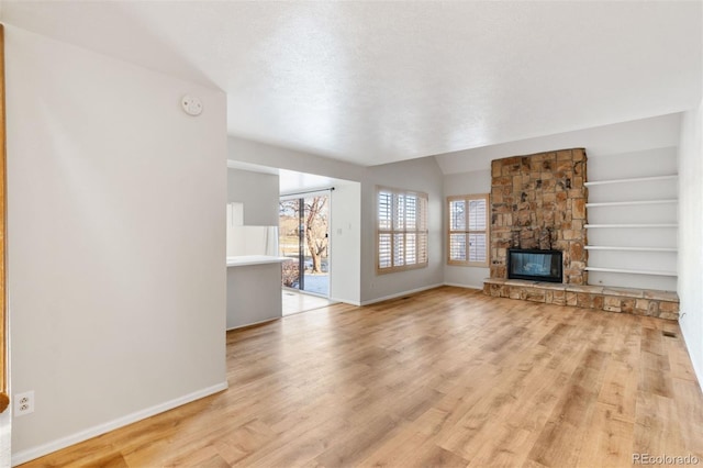 unfurnished living room featuring a fireplace, built in features, a wealth of natural light, and light hardwood / wood-style floors