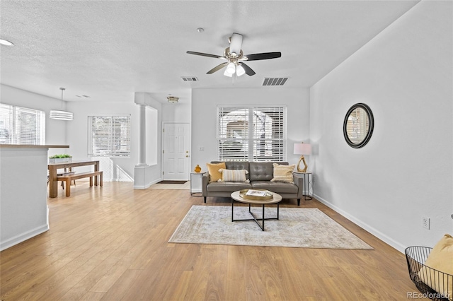 living room with plenty of natural light, light wood-style floors, decorative columns, and visible vents