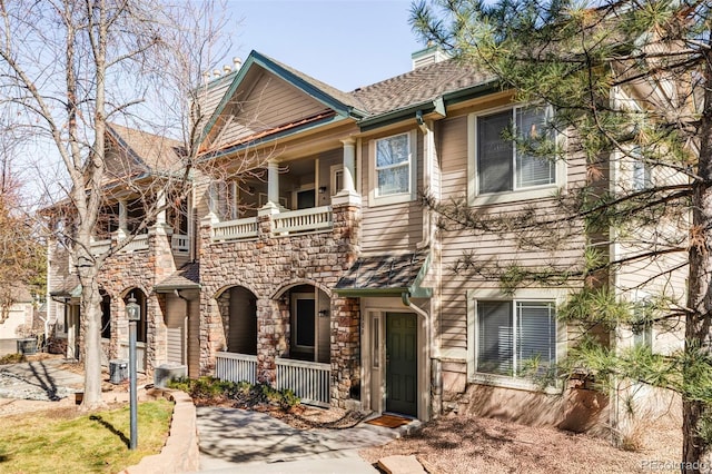 view of front of home featuring a porch, a chimney, stone siding, and a balcony