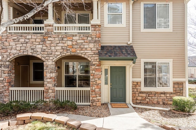 exterior space featuring stone siding, a shingled roof, and a porch