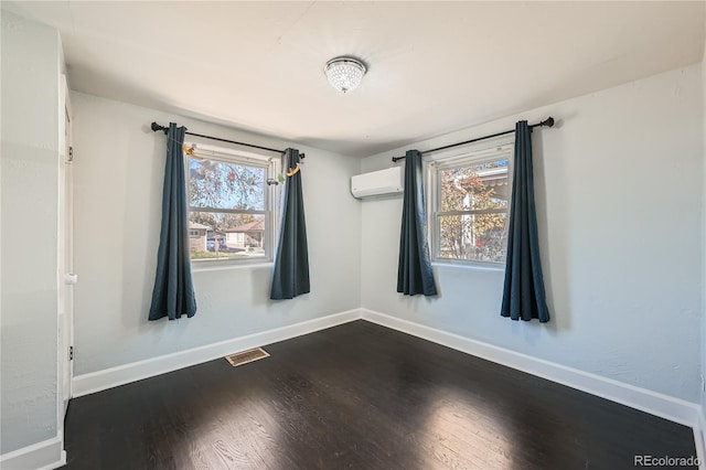 spare room featuring an AC wall unit, a healthy amount of sunlight, and dark hardwood / wood-style floors