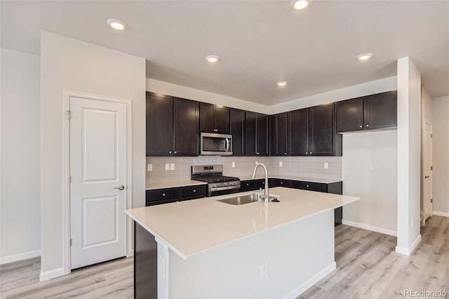 kitchen featuring stainless steel appliances, a kitchen island with sink, sink, and light wood-type flooring