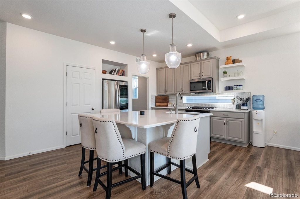 kitchen with gray cabinets, decorative light fixtures, dark hardwood / wood-style floors, appliances with stainless steel finishes, and a kitchen island with sink