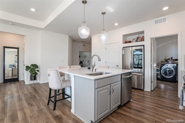 kitchen with gray cabinetry, sink, dark hardwood / wood-style floors, washer / clothes dryer, and a kitchen island with sink