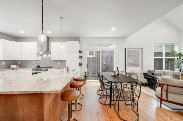 1947 King St, Denver, CO 80204 - kitchen featuring wall chimney exhaust hood, stainless steel range, modern cabinets, light wood-style floors, and a breakfast bar