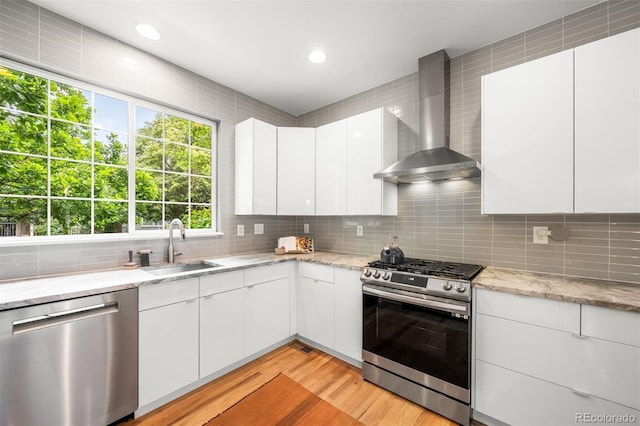 1947 King St, Denver, CO 80204 - kitchen featuring appliances with stainless steel finishes, wall chimney range hood, a sink, decorative backsplash, and light wood finished floors