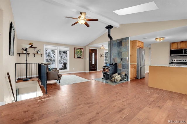 living room featuring vaulted ceiling with skylight, ceiling fan, light hardwood / wood-style floors, and a wood stove