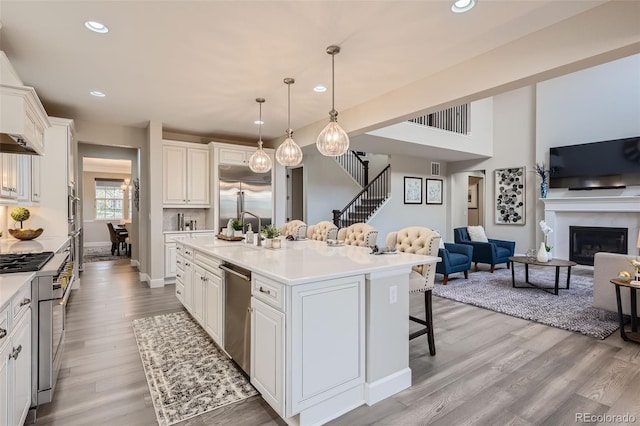 kitchen with decorative light fixtures, appliances with stainless steel finishes, light hardwood / wood-style floors, white cabinetry, and an island with sink